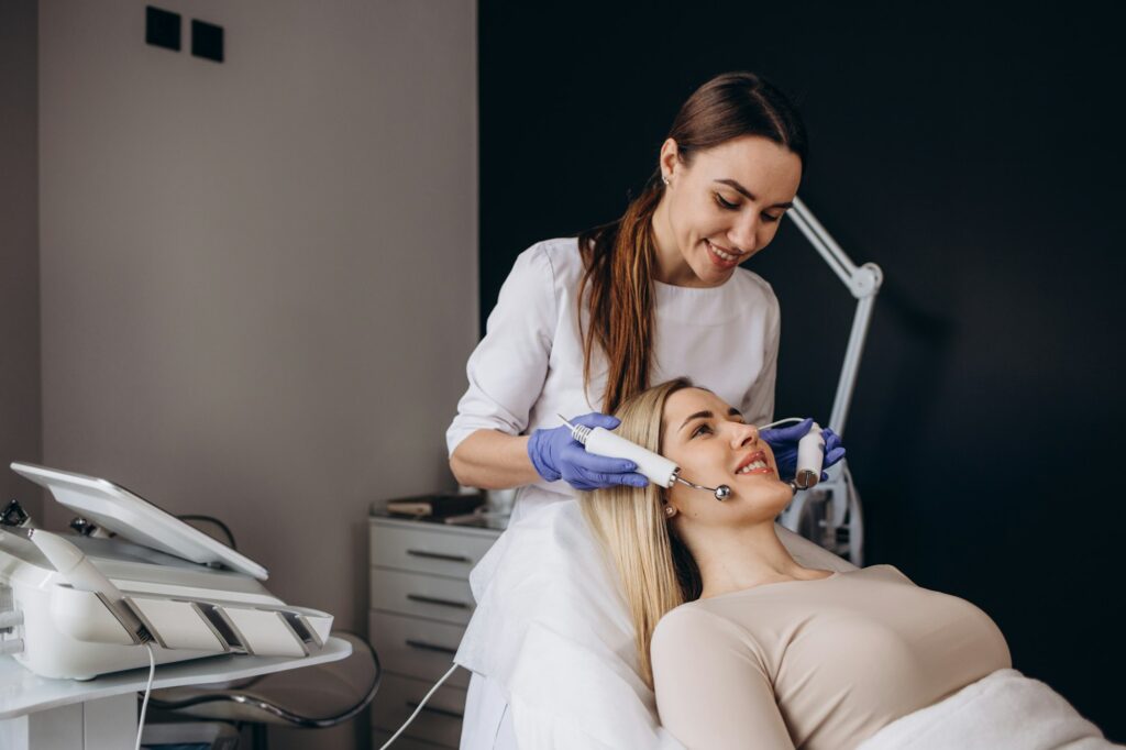 A doctor cosmetologist makes a microcurrent facial therapy to a young woman with a device