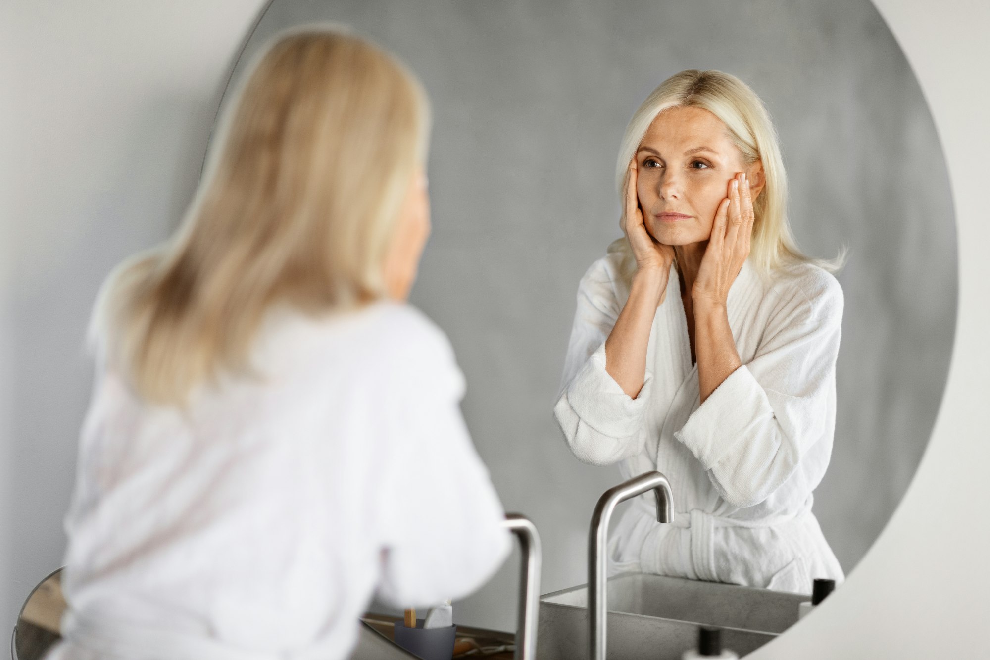 Aging Signs. Upset senior woman looking in mirror in bathroom
