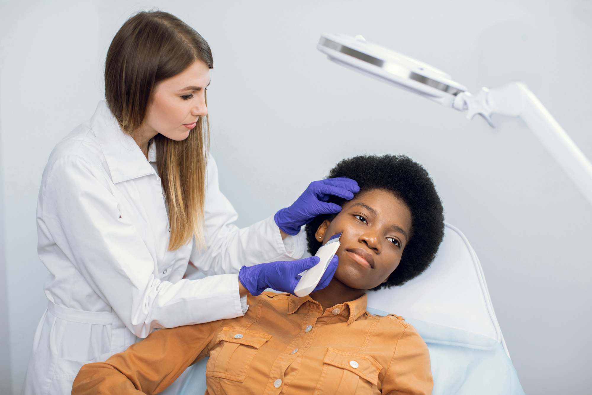Beauty and face care concept. Female doctor cosmetologist in blue gloves makes ultrasound cleaning