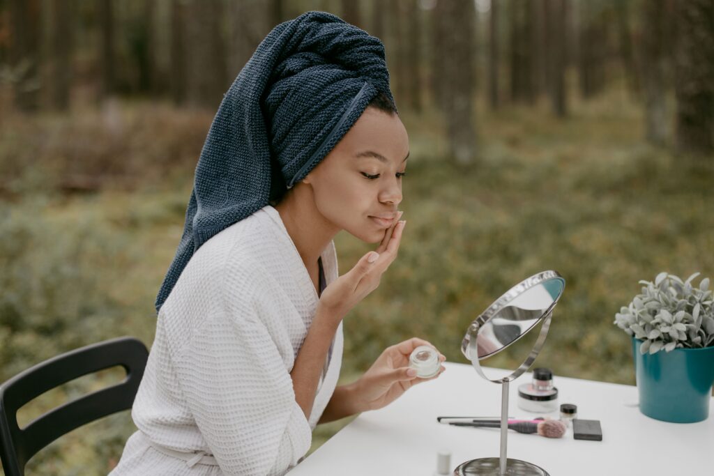 Person applying facial moisturizer as part of a daily skincare routine while looking in a mirror outdoors.