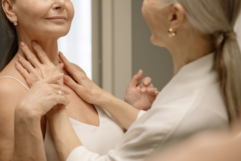 Mature woman examining loose neck skin and signs of aging in a mirror.