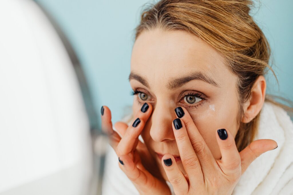 Woman applying eye cream to the under-eye area as part of a daily anti-aging skincare routine.
