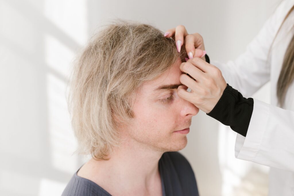 Healthcare professional examining a male patient's forehead during a facial aesthetics consultation or cosmetic treatment assessment.