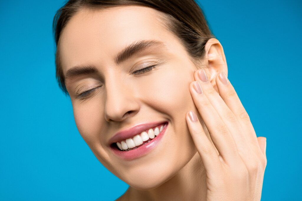 Smiling woman with clear, radiant skin gently touching her face, highlighting a healthy complexion and skincare results.