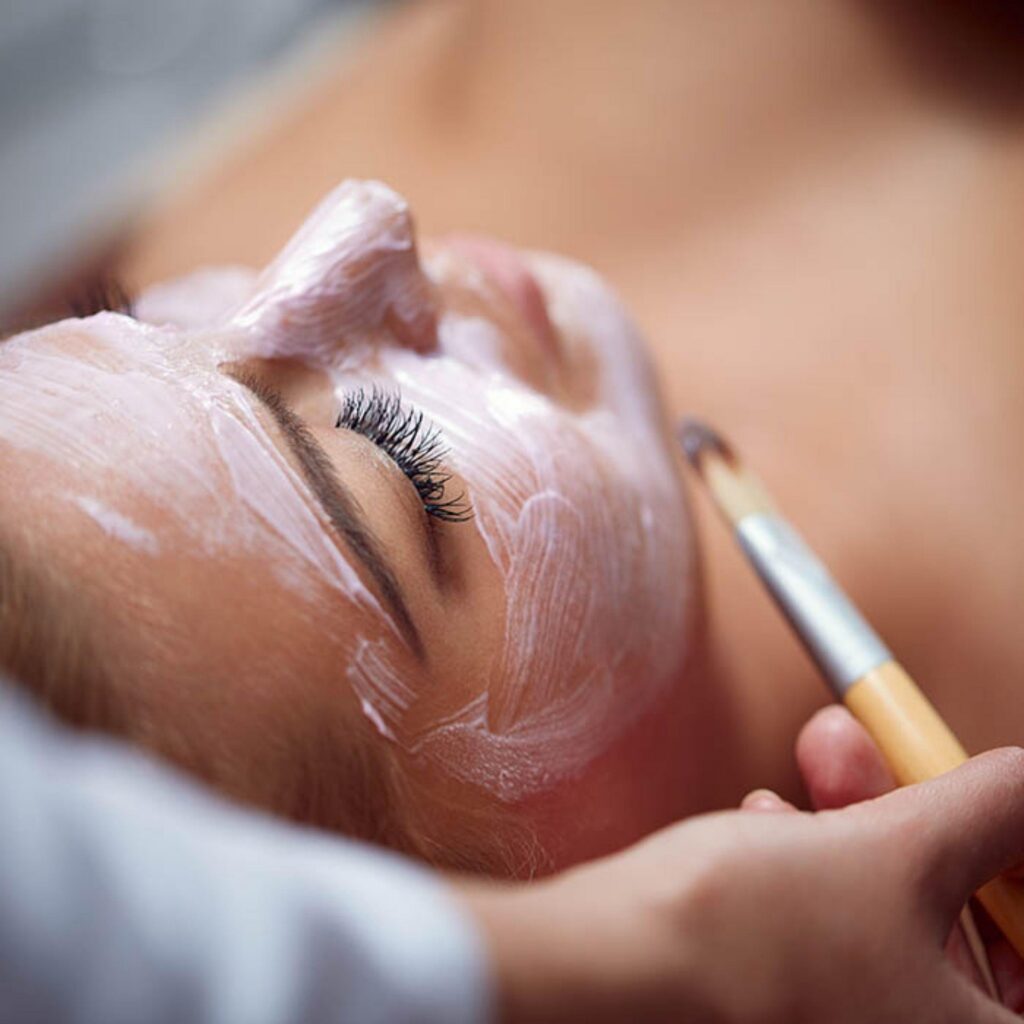 Professional applying a nourishing facial mask with a brush during a relaxing spa skincare treatment.